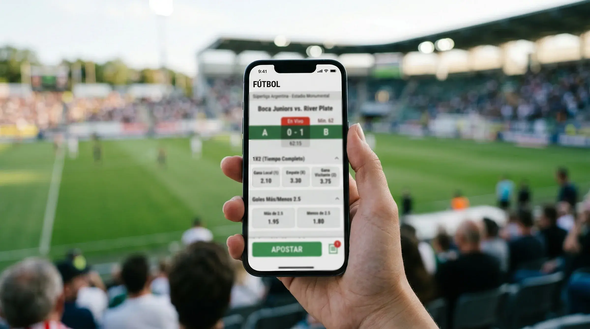 Mano sosteniendo un celular con una app de apuestas deportivas frente a una cancha de fútbol